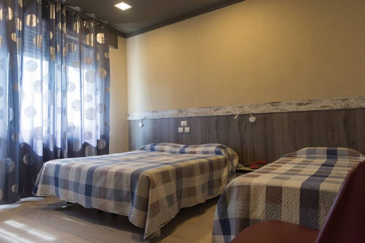 A room with two beds, a wooden headboard, and a window with patterned curtains.