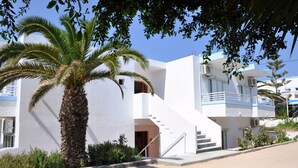 A modern building with a white exterior, a palm tree, and a staircase leading to an upper level. - Haralambos Studios (Kos)