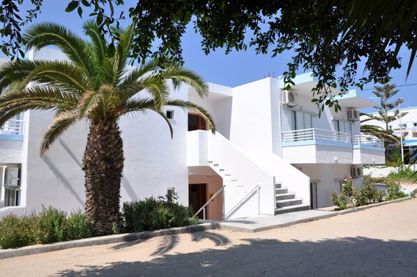 A modern building with a white exterior, a palm tree, and a staircase leading to an upper level. - Haralambos Studios (Kos)