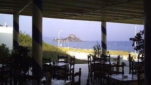 An outdoor dining area with tables and chairs, overlooking a beach and the sea. - Haralambos Studios (Kos)
