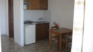 A compact kitchen with wooden cabinets, a white refrigerator, and a dining table with a chair. - Haralambos Studios (Kos)