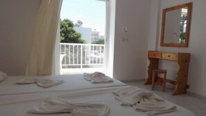 A hotel room with two beds, a wooden desk, a mirror, and a balcony with a white railing. - Haralambos Studios (Kos)