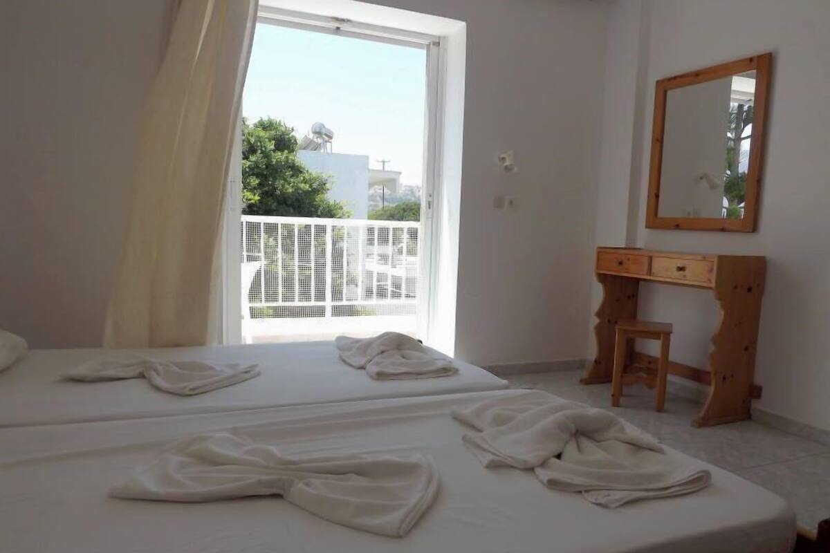 A hotel room with two beds, a wooden desk, a mirror, and a balcony with a white railing.