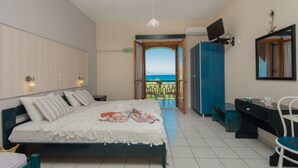 A bedroom with a bed, a desk, a chair, a TV, and a view of the sea. - Kavos Psarou Studios and Apartments (Zakynthos)