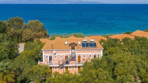 A two-story building with a balcony, solar panels, and a view of the sea and mountains. - Kavos Psarou Studios and Apartments (Zakynthos)