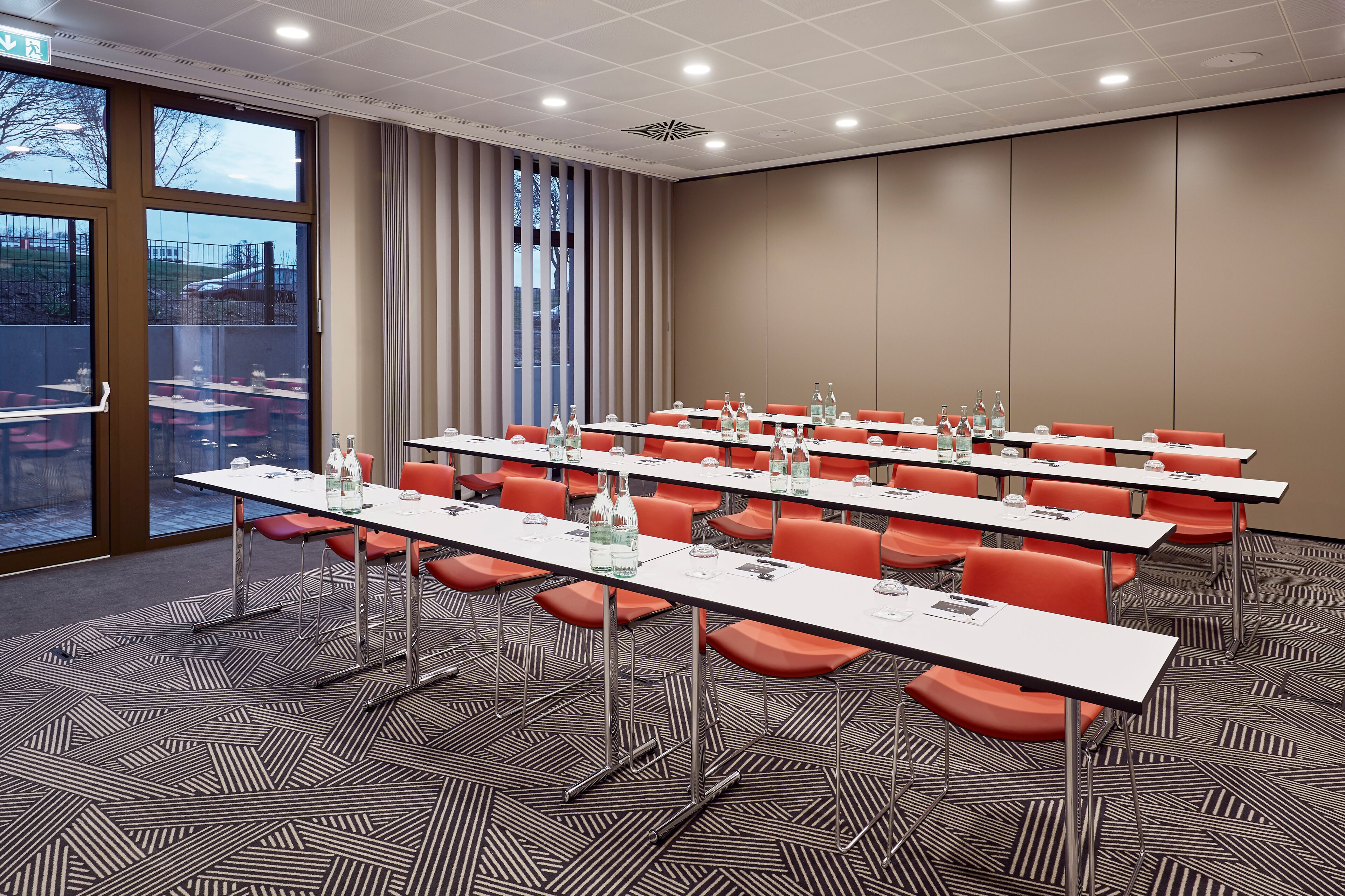 A conference room with multiple tables and chairs, large windows, and a patterned carpet.
