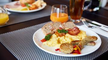 Une assiette de petit-déjeuner comprenant des œufs brouillés, des saucisses et des toasts, accompagnée d’un verre de jus d’orange et d’une tasse de thé.