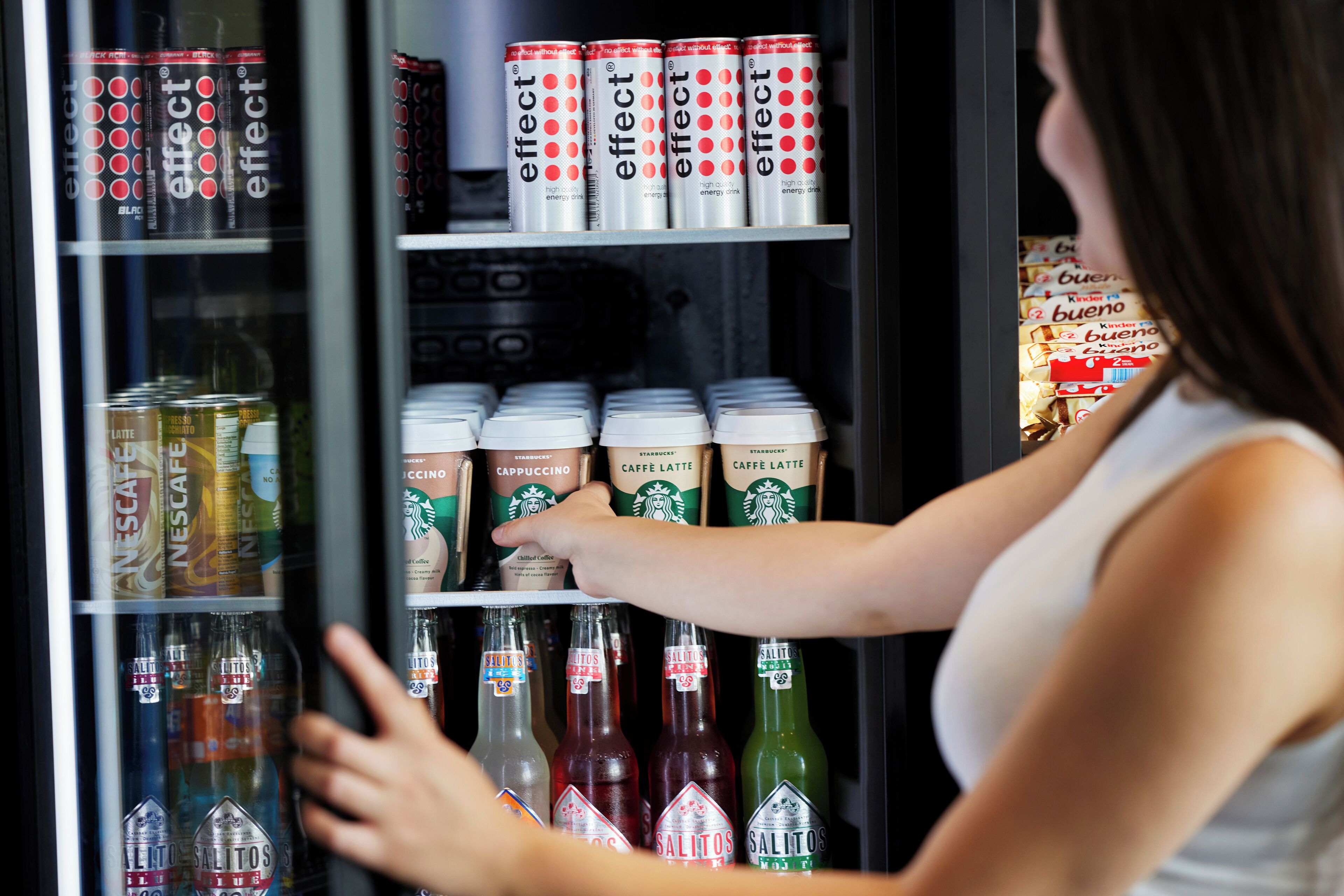 A beverage refrigerator stocked with various drinks including Nescafe, Starbucks, and Salitos.