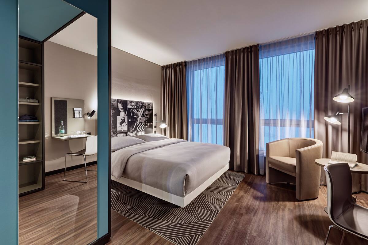 Una habitación de hotel moderna con una cama grande, un escritorio, una silla y vistas al exterior.