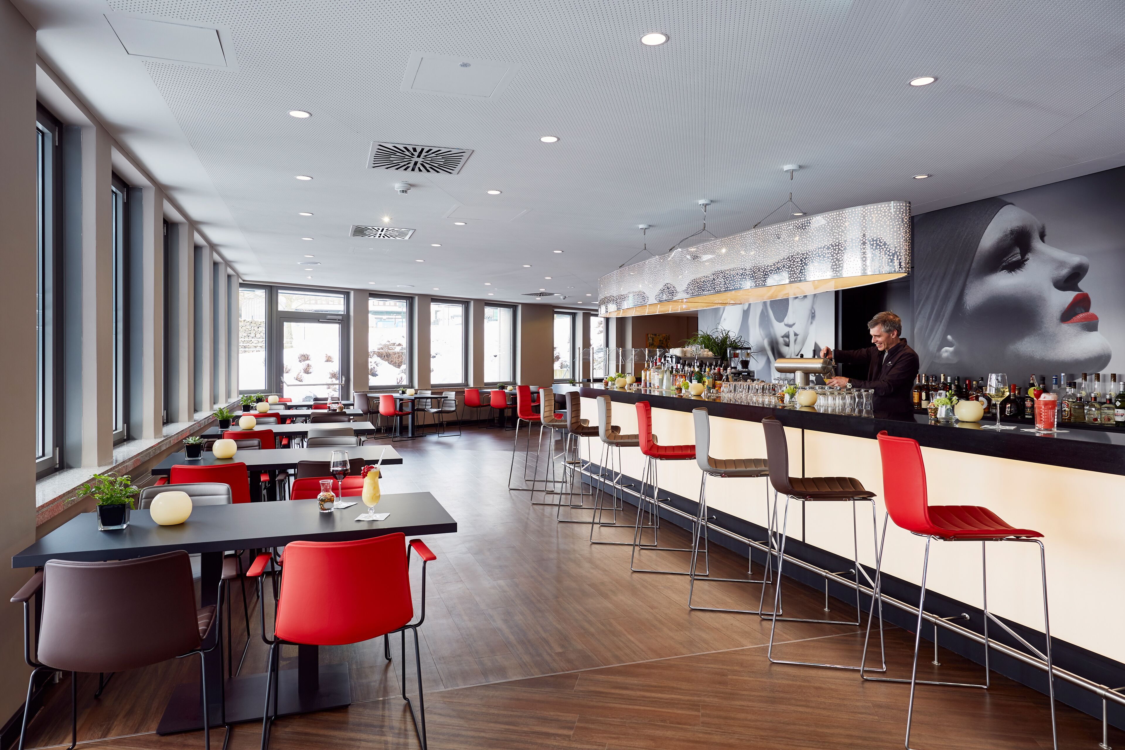 A modern bar area with a long counter, red and brown bar stools, and a bartender.