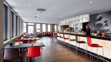 A modern bar area with a long counter, red and brown bar stools, and a bartender.