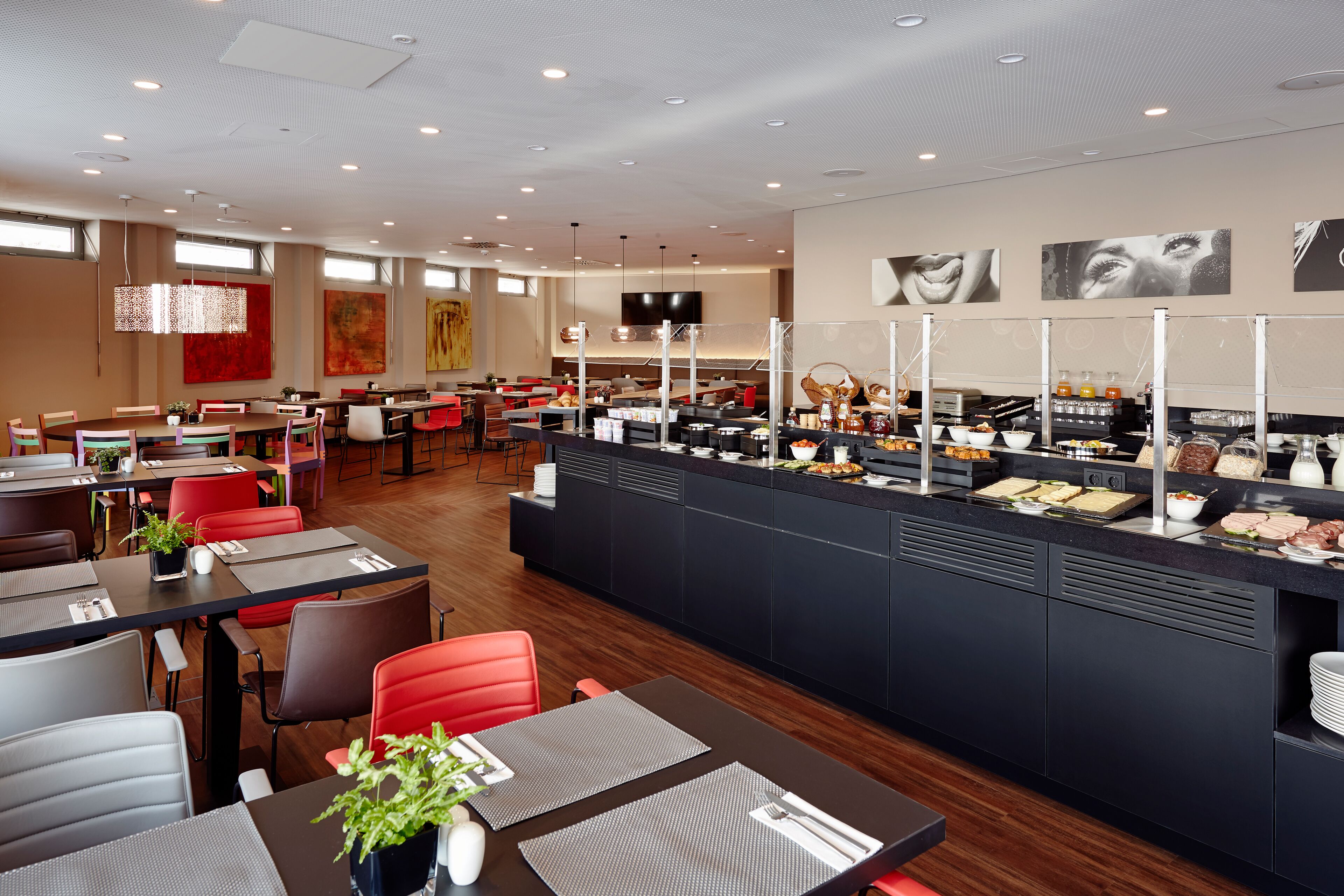 Ein modernes Restaurant mit mehreren Tischen, einer Buffettheke und einem Flachbildfernseher an der Wand.