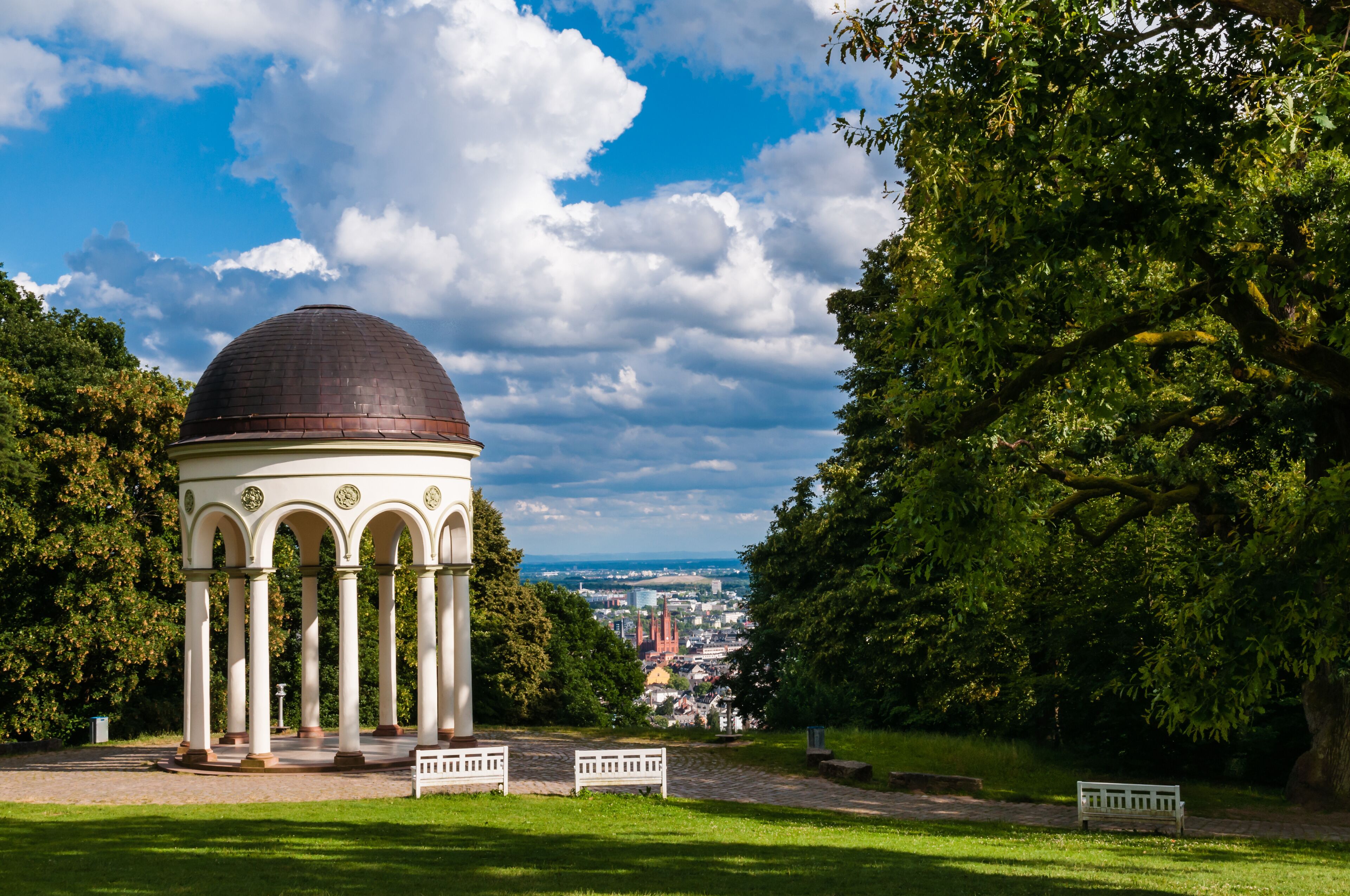 A gazebo with a dome roof, surrounded by lush greenery and benches.