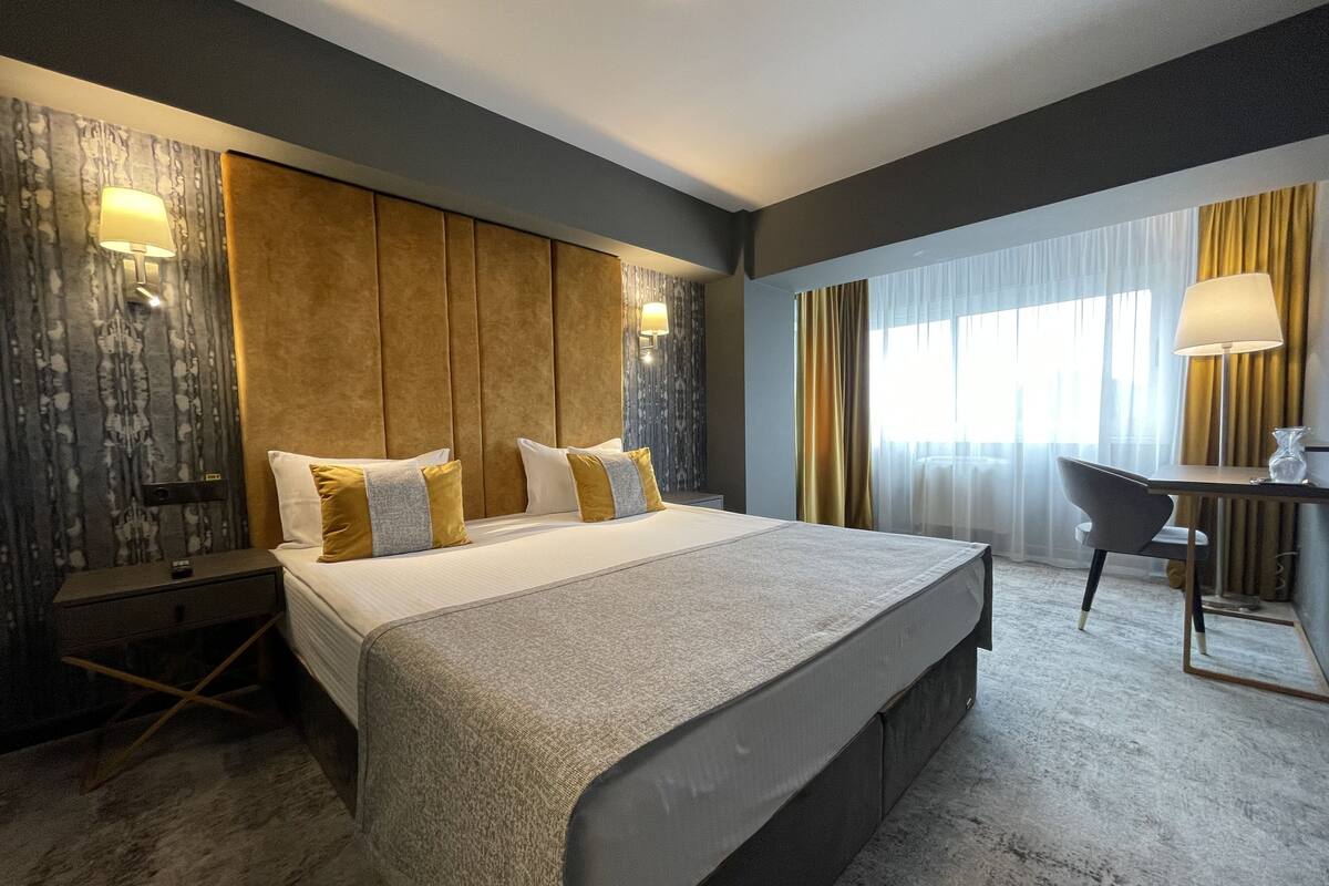 A hotel room with a large bed, bedside tables, a desk, and a chair.