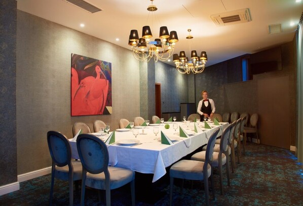 A conference room with a long table set for a meeting, surrounded by chairs, and a large painting on the wall.