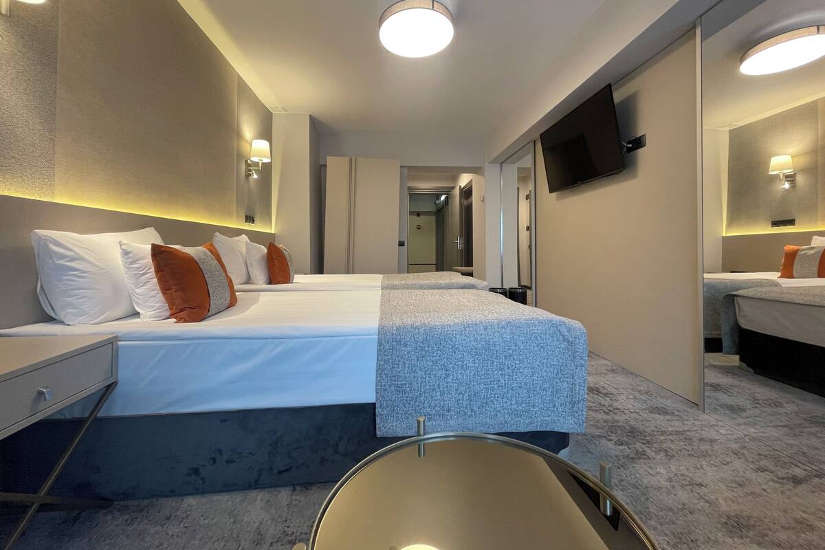 A hotel room with a large bed, bedside tables, a flat-screen TV mounted on the wall, and a mirror.