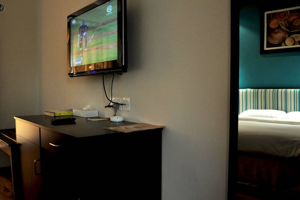 Habitación de hotel con una televisión montada en la pared, una mesita de noche con un control remoto, una caja de pañuelos y un cuadro enmarcado en la pared.