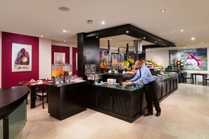 A buffet setup with a server, a counter with food containers, and a wall with a poster. - Al Wadi Hotel Sohar (Sohar)
