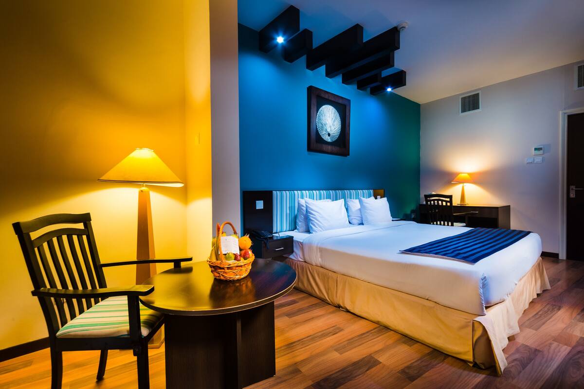 Una habitación de hotel con cama, mesita de noche, silla y lámparas.