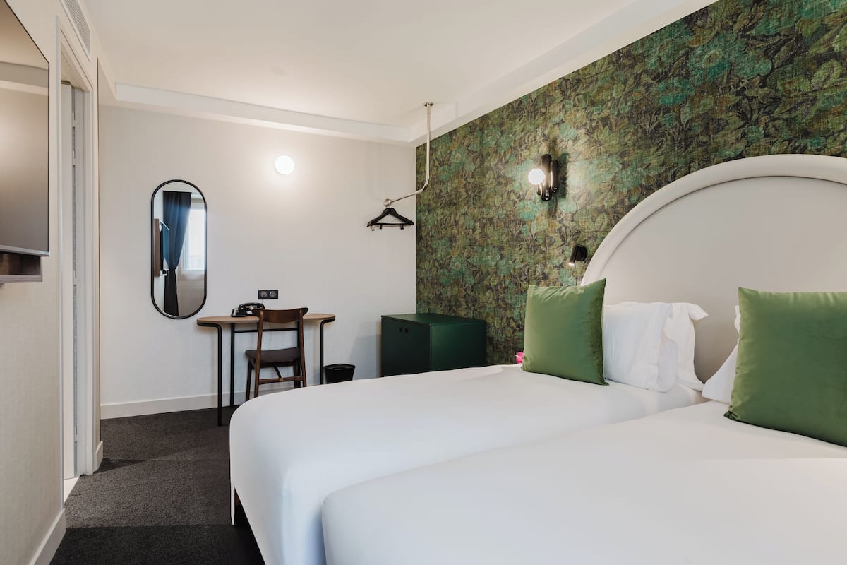 A hotel room with a large bed, a desk, a chair, a mirror, and a wardrobe.
