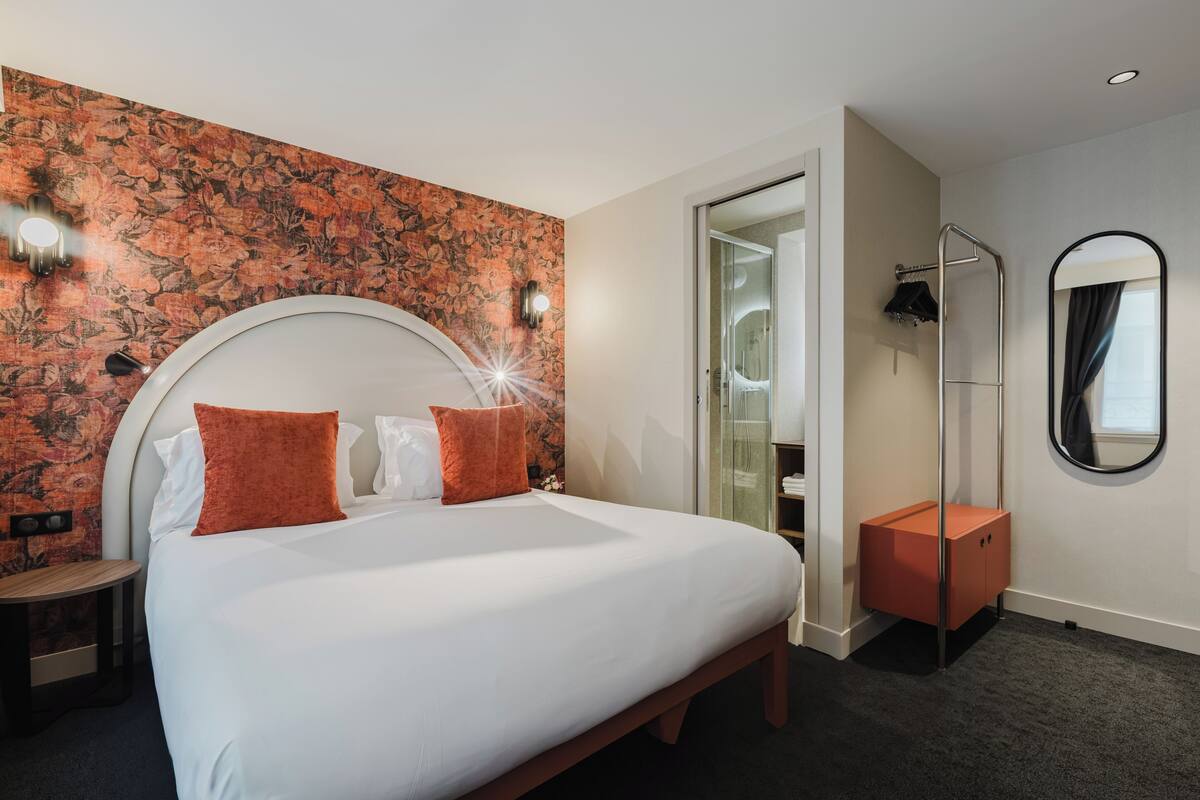 A hotel room with a large bed, a wooden nightstand, a mirror, and a shower area.