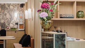 A reception area with a wooden desk, a vase of flowers, a 'RECEPTION' sign, and a wall-mounted device. - Prince Albert Opera (Paris)