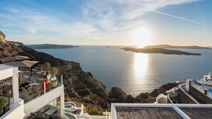 A coastal hotel with a terrace overlooking the sea, featuring outdoor seating and a view of the sunset. - Petit Palace (Santorini)