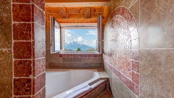 A bathroom with a bathtub, a window with a mountain view, and a tiled wall.