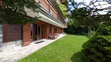 A two-story wooden building with a stone foundation, a covered patio with outdoor furniture, and a well-maintained lawn.