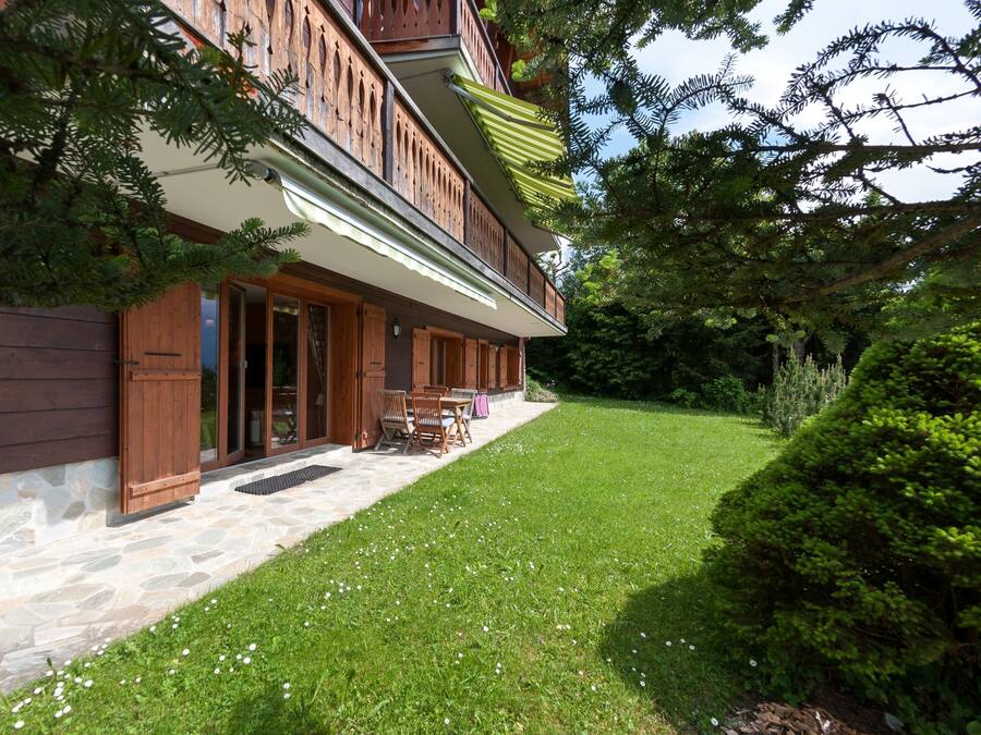 A two-story wooden building with a stone foundation, a covered patio with outdoor furniture, and a well-maintained lawn.