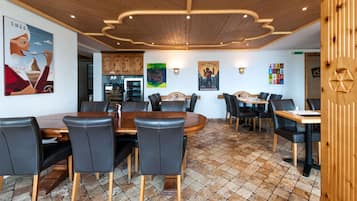 A dining area with a wooden ceiling, tiled floor, and black leather chairs. There are posters on the walls and a wooden panel on the right.