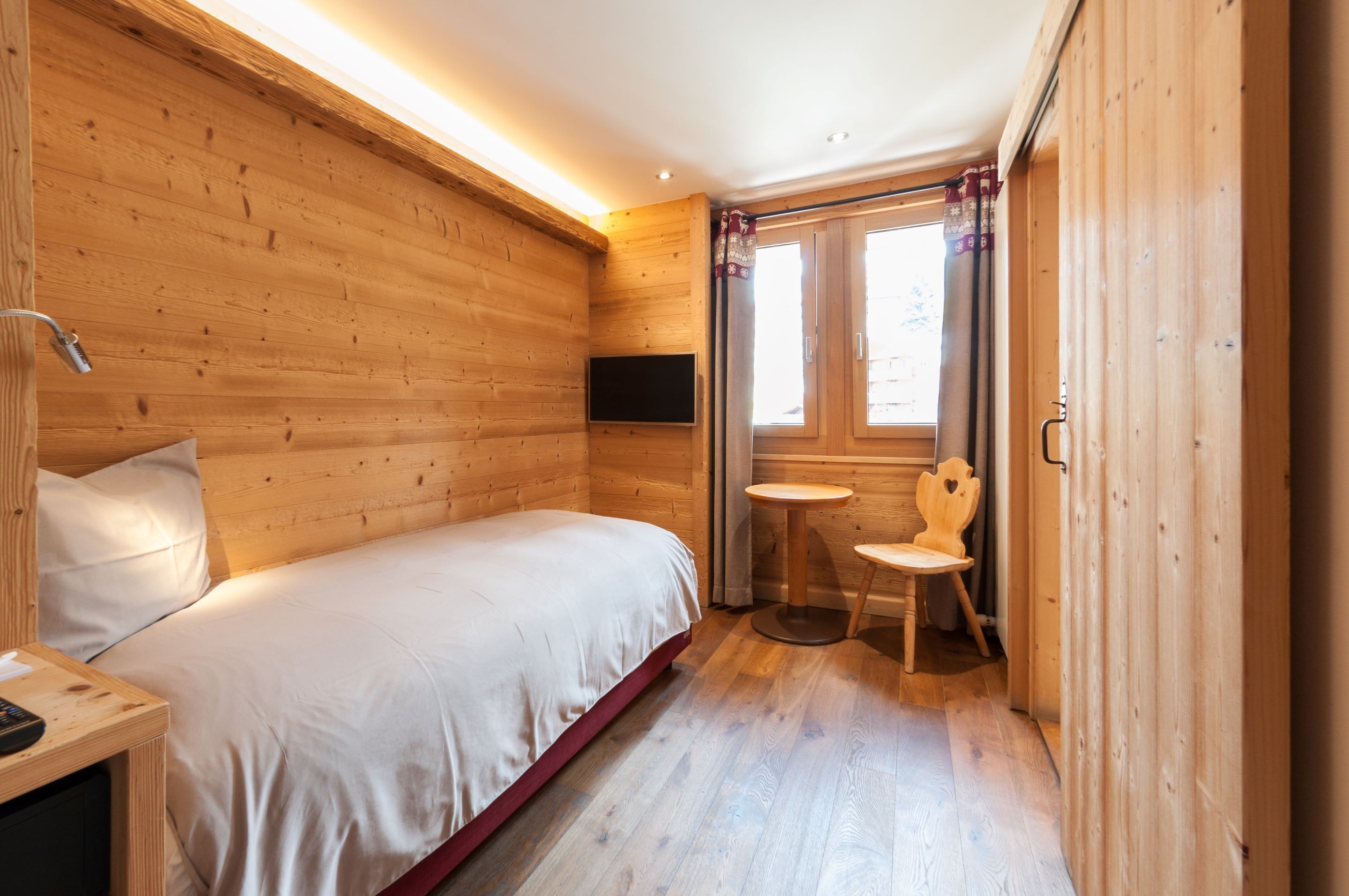 Una habitación de madera con una cama, una mesita y una silla.