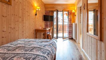 A wooden room with a bed, a desk, and a TV. There is a sliding glass door leading to an outdoor area.