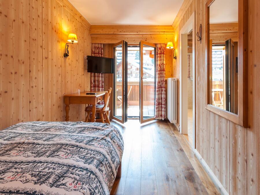 A wooden room with a bed, a desk, and a TV. There is a sliding glass door leading to an outdoor area.
