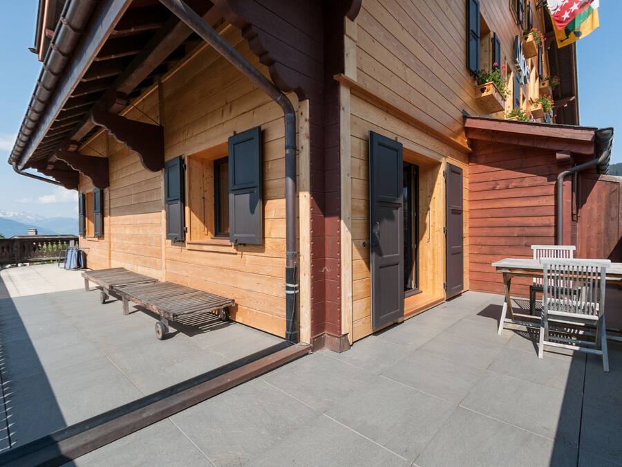 A wooden building with a balcony, a table with chairs, and a bench.