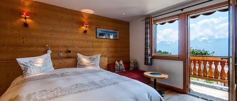 Een slaapkamer met een groot bed, houten paneelwanden, een klein tafeltje en een balkon met uitzicht.