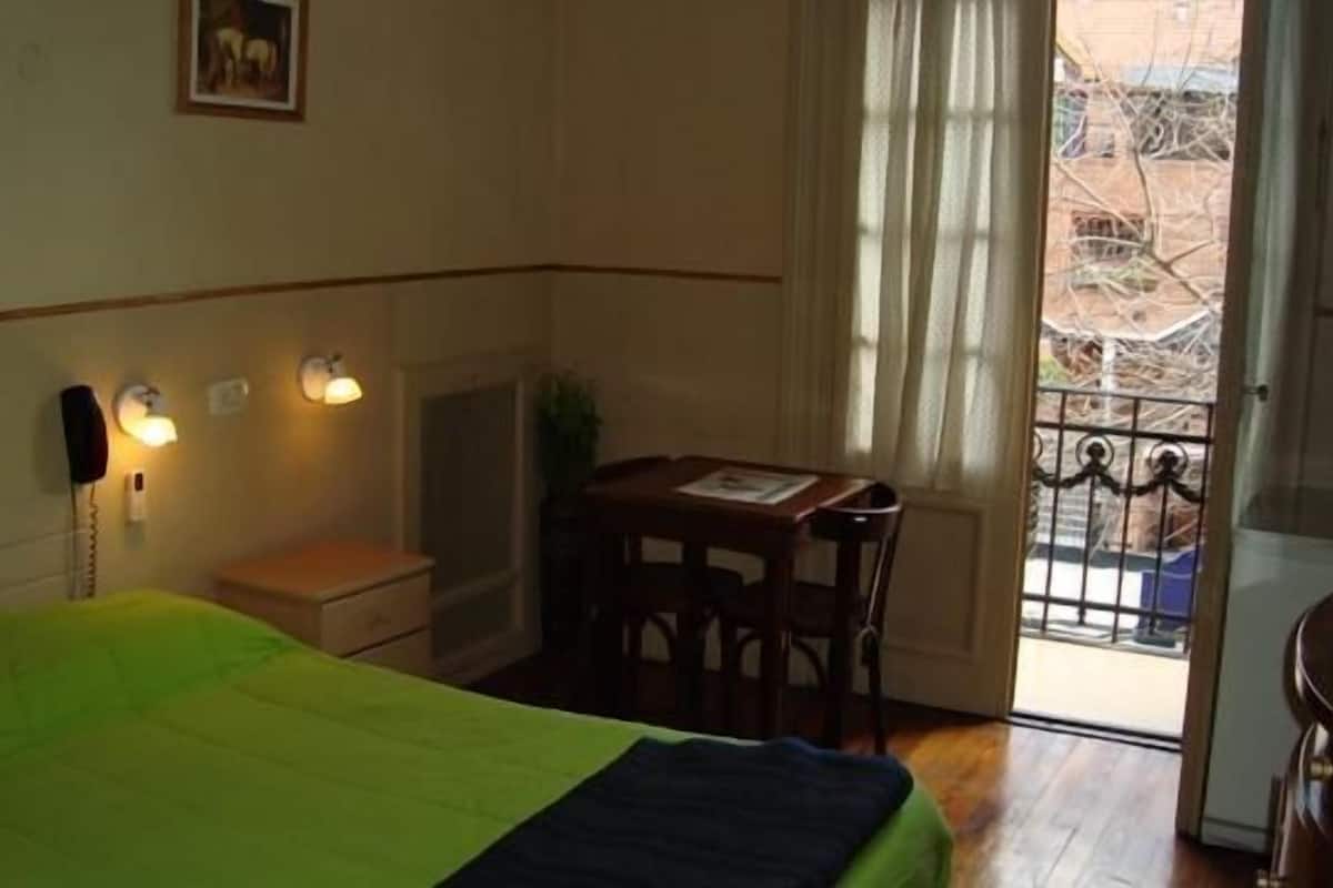 A hotel room with a bed, a desk, and a window with a view of the outside.