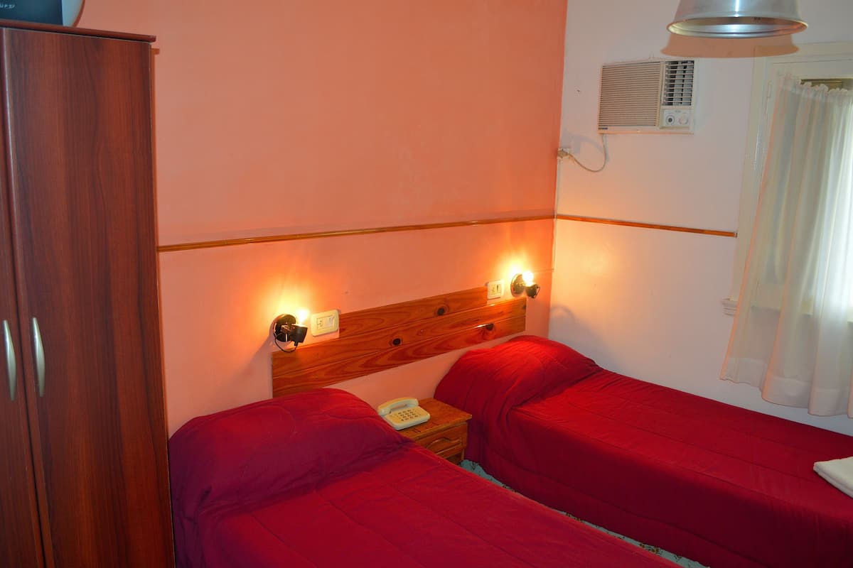 A room with two beds, a wooden wardrobe, a bedside table with a phone, and a wall-mounted heater.