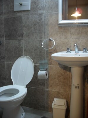 A bathroom with a toilet, sink, and a trash bin. - De la Rue (Buenos Aires)