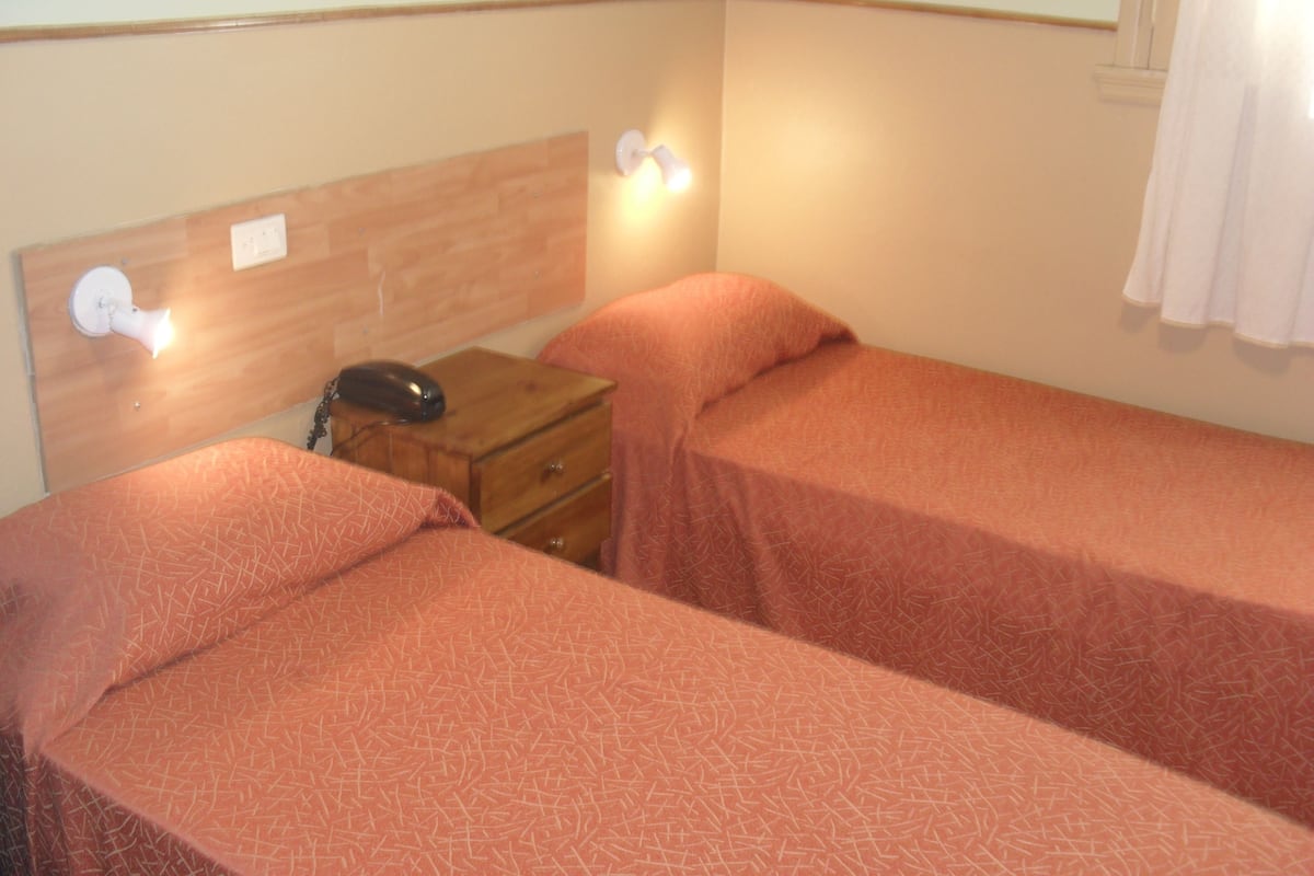 A room with two single beds, a wooden nightstand with a telephone, and wall-mounted lights.