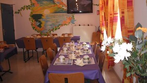 A dining area with a long table set for a meal, chairs around it, a television on the wall, and a decorative painting above the table.