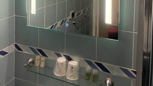 A bathroom with a large mirror, a glass shelf with toiletries, and a shower area.