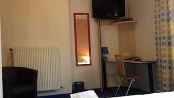 A hotel room with a bed, a desk, a chair, a television, a radiator, and a mirror.