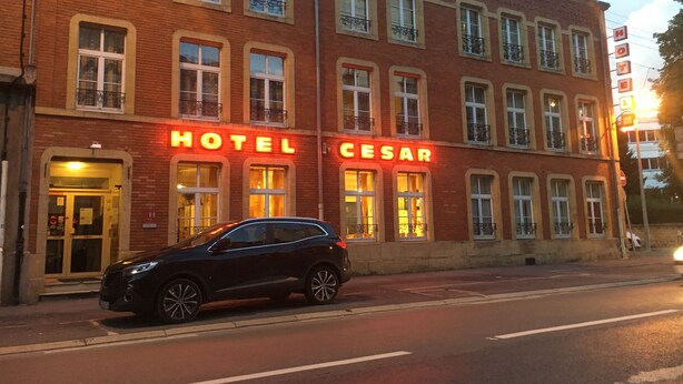 A hotel with a red facade and illuminated signage reading "HOTEL CESAR".