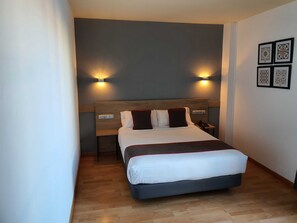 A modern hotel room with a large bed, two bedside tables, a nightstand, and wall-mounted lighting. - Hospedium Hotel Vittoria Colonna (Medina de Rioseco)