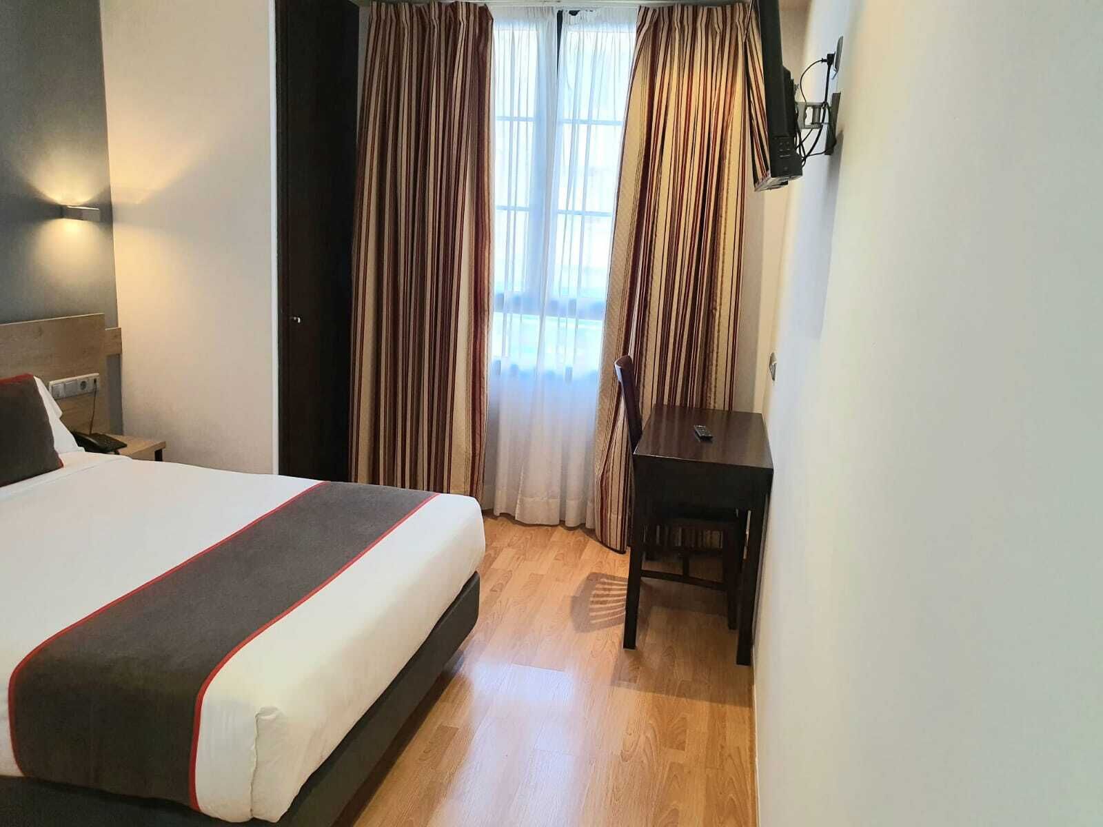 Una habitación de hotel con una cama, un escritorio y cortinas.