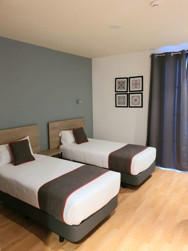 Two single beds with headboards, a wall-mounted light, and four framed wall art pieces.