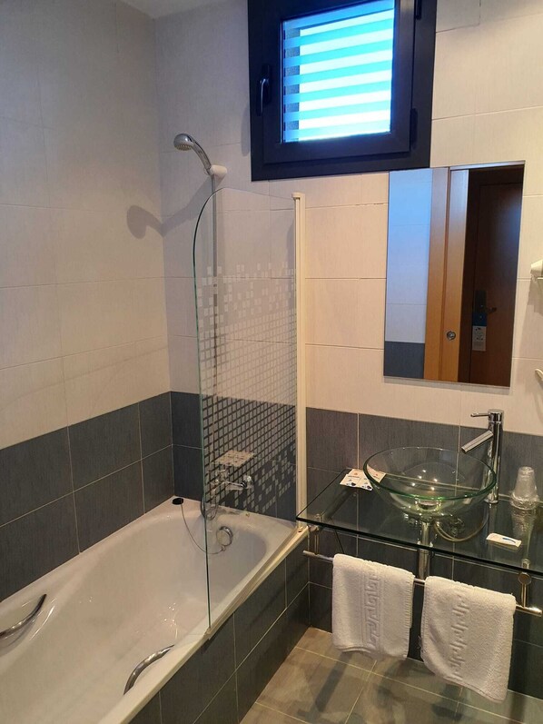 Un baño moderno con ducha envuelta en vidrio, lavamanos de vidrio y bañera.