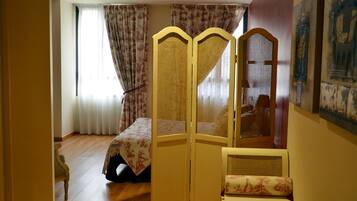 Una habitación con una cama, una silla, un biombo decorativo y un cuadro en la pared.