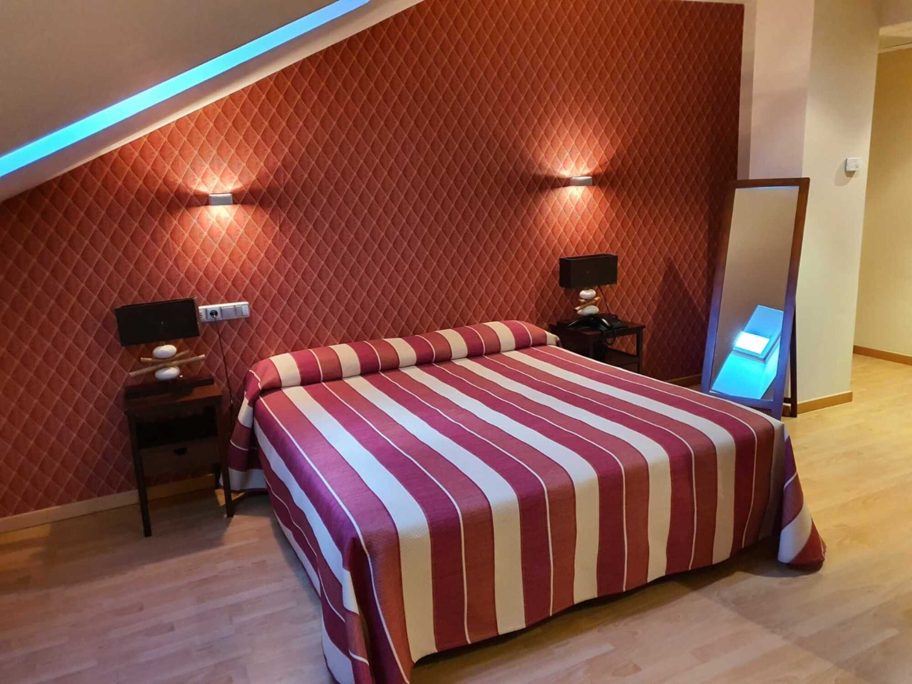 A bedroom with a sloped ceiling, a bed with a striped bedspread, two bedside tables with lamps, and a mirror on the wall.